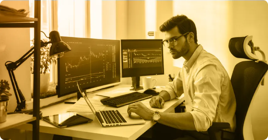 A man at a desk with dual monitors and a laptop, engaged in learning about opening a Forex trading account.